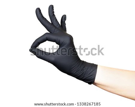 Female hand in black glove shows ok sign on a white background. The thumb and index fingers are closed in a ring, the other three fingers are raised up. Back view
