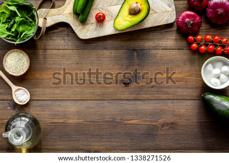 Ingredients for fresh vegetable salad and cutting board on dark wooden kitchen desk top view copy space