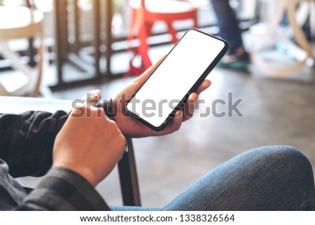 Mockup image of woman's hand holding black mobile phone with blank white desktop screen in cafe