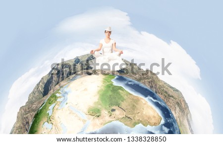 Young woman keeping eyes closed and looking concentrated while meditating on clouds in the air with panoramic view of Earth globe on background. Elements of this image are furnished by NASA