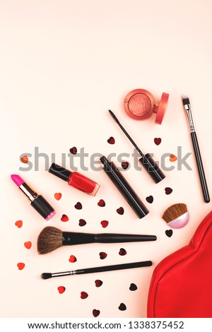 Beauty and makeup products spilling out of a cosmetics bag on a coral background. Decorated with heart shape confetti. Flat lay, top view. Copy space. Vertical shot.