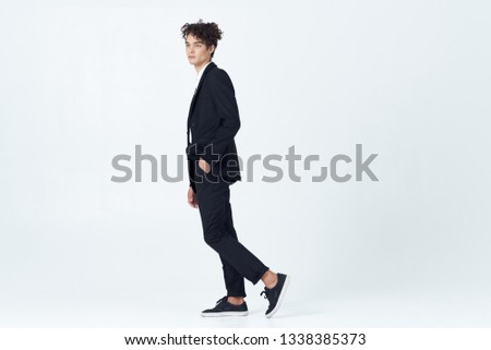 Curly guy in a classic suit in full growth on a light background                          