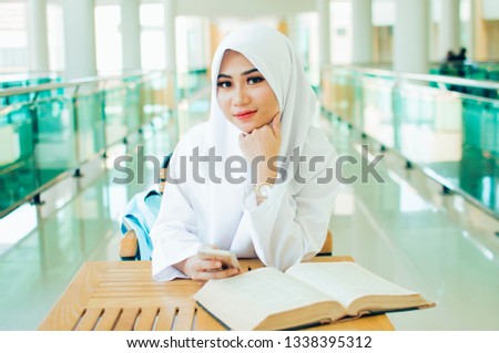 Little muslim girl wearing hijab and doing homework in class. Young arab schoolgirl in chador writing during exam in classroom. 
