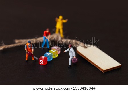 Discount sale concept. Miniature people work with the label for clothes. Close up. 