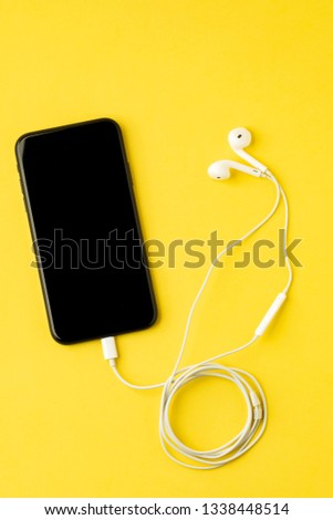 Smartphone with headphones on yellow background. Listen to music.