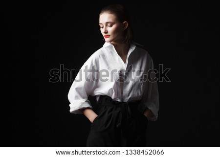 Portrait of an elegant young woman in a white shirt and black pants. Interesting studio light. Black background