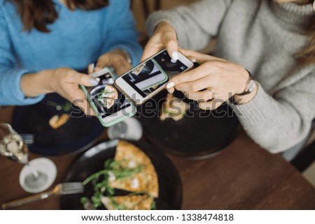 Two bloggers taking photos for social media in cafe. Focus on women's hands holding mobile phones and using 
photography application.