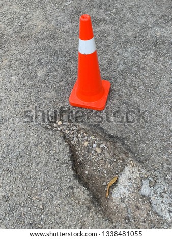 pothole damage with traffic cone on road. Image contain certain grain or noise and soft focus.