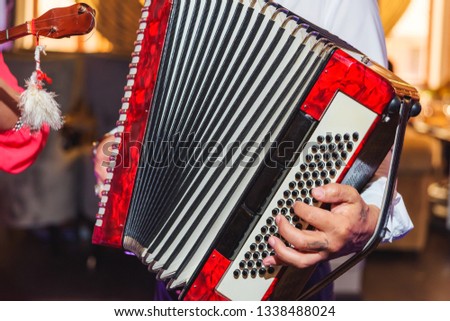 A man plays a red accordion. Musical instrument.  The event at the restaurant. Black round buttons. Hand harmonica. The woman in the pink dress.