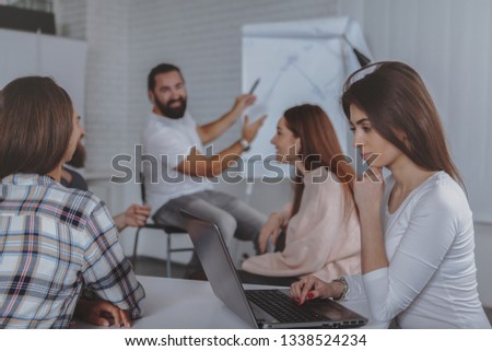 Beautiful woman using her laptop duing business meeting with colleagues at the office. Bearded mature businessman leading meeting of creative team of designers