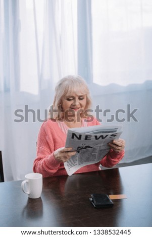 senior woman sitting at table and reading newspaper at home with copy space