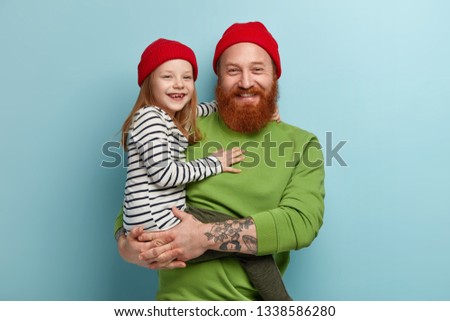 Cheerful stylish father with foxy beard holds little smiling daughter on arms have fun, play together, pose for making family portrait, have ginger hair, look similar. Parents, children, relationship Royalty-Free Stock Photo #1338586280