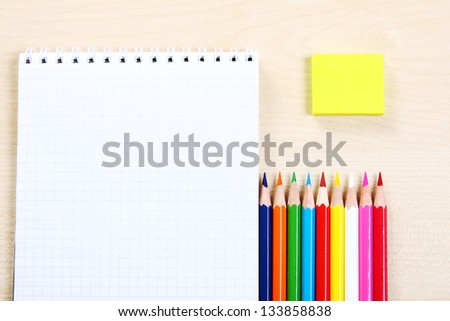 A row of multicolored pencils with a open empty notepad and a yellow eraser