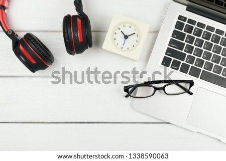 Table top view of office desk with laptop, clock, and headphone on white wooden desk