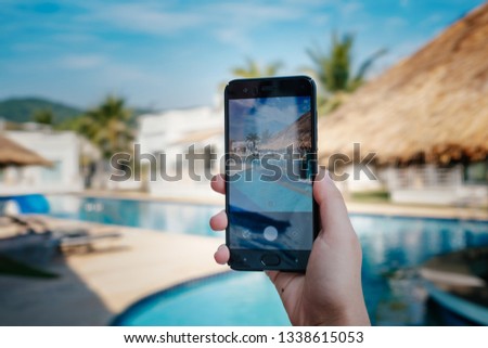 hand holding phone on background of the pool in hotel. photo camera on the screen. close up hand hold smartphone take a picture of summer vacation