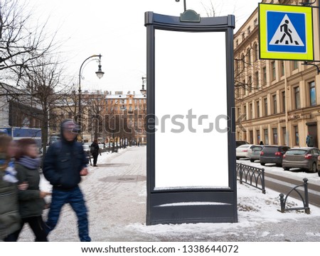 Vertical city billboard with white field MOCKUP. In the city center in the afternoon with snow in the winter. with blurred people passing by