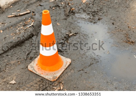 close-up of striped plastic orange parking cone on wet ground with car tracks, puddles and orange leaves. Warning orange cone on the сonstruction site, springtime
