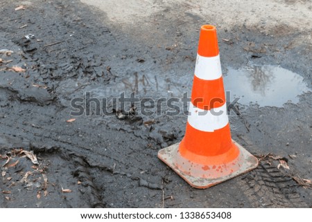close-up of striped plastic orange parking cone on wet ground with car tracks, puddles and orange leaves. Warning orange cone on the сonstruction site with copy space background, selective focus
