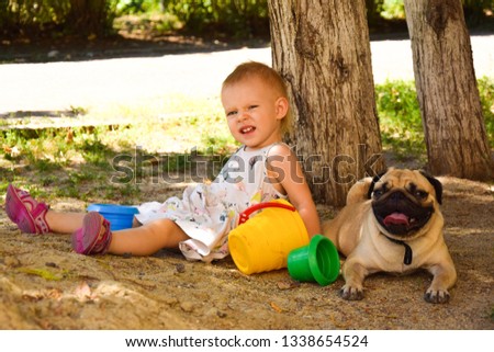 Little girl playing outdoors with her puppy pug. Girl and a dog.