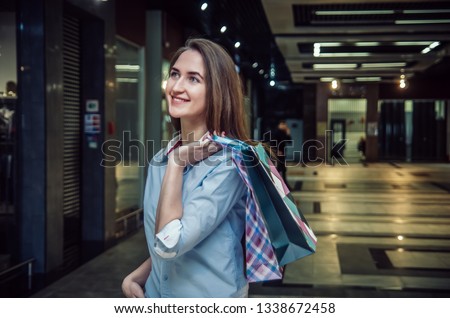 Beautiful young brown-haired girl with long hair with a lot of packages on the shoulder in a mall. Cheerful, happy shopping girl