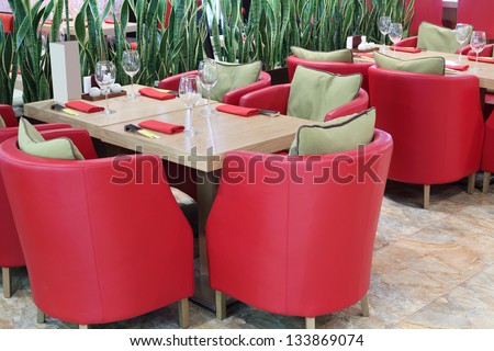 Tables with glasses, soft red armchairs in small modern Japanese restaurant.