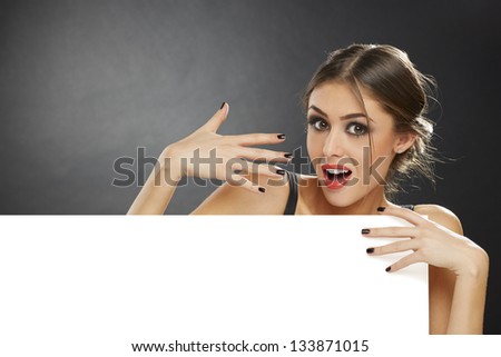 Portrait of a surprised young girl holding blank billboard against dark background.