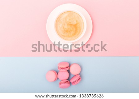 Cup of coffee with macaron on pink and blue background from above, flat lay