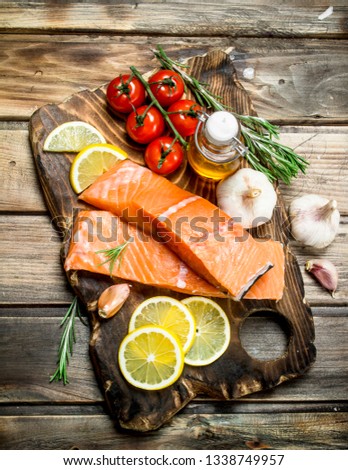 Raw salmon fish filet with lemon, tomatoes and herbs. On a wooden background.
