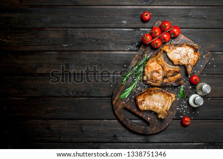 Grilled pork steaks with rosemary and fresh tomatoes. On a wooden background.