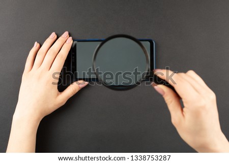 search in the phone with a magnifying glass in the hands on a black background, top view. search engine concept. spying mobile smart phone