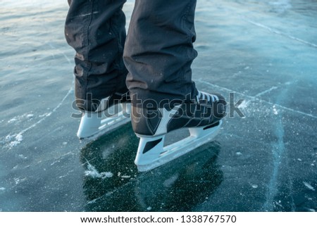 Men's feet skating on the clear ice of lake Baikal. Ice skating in nature at sunset in winter. Travel and sports