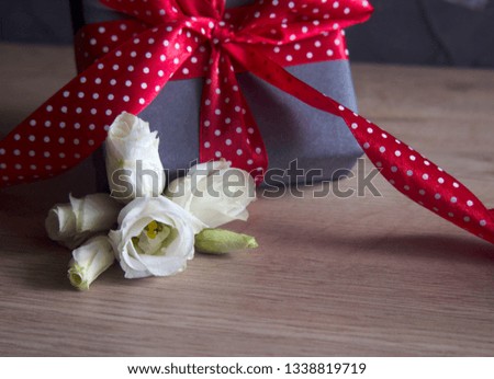 White flowers (eustoma) and a gray gift box with red ribbon in white beans (dots) on a dark wooden background