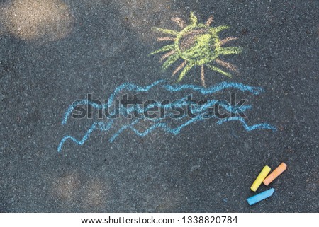 Drawing of blue sea water and yellow sun on pavement of sidewalk outdoors at city park. Child drawing tropical beach. Horizontal color photography.