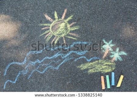 Closeup top view of child's chalk drawing of tropical beach. Blue sea water, yellow sun, sandy island with green palms growing painted at sidewalk outdoors at city park. Horizontal color photo.