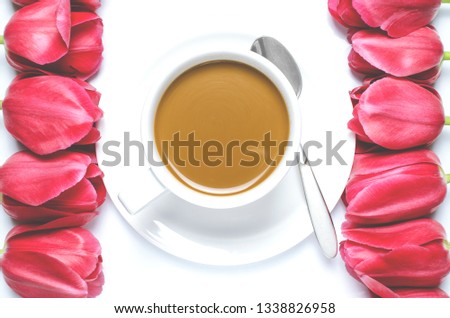 White coffee cup stands on a white plate with white background near multi-colored tulips