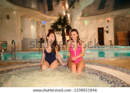 close up photo of  two beautiful women wearing swimsuits relaxing in swimming pool