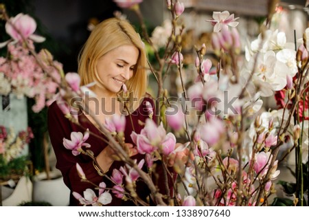 Happy blond woman standing among beautiful blooming magnolia flowers on the tree branch