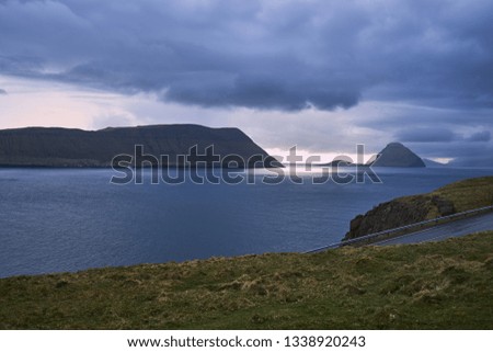 Scenic landscape Picture of great fjord in Faroe island Stremoy during day with heavy clouds and sun rays goes to the water. Typical scandinavian coastline without trees and weather during the spring.