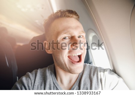 Happy tourist man makes selfie photo in cabin aircraft airplane before departure. Travel concept.