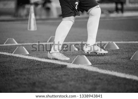 Black and white picture of Soccer player Jogging and jump between cone markers on green artificial turf for soccer training. Football or Soccer Academy.
