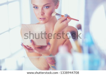 A picture of a young woman applying face powder in the bathroom