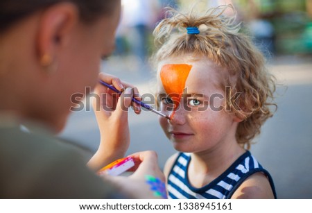 boy face close-up with red colors on his face, face painting watercolor, artist paints watercolor paints tiger mask, draw on the boy's face paints picture, orange ink for drawing the tiger.