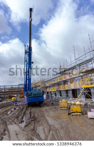 Crane on a Muddy Building Site with Scaffolding Surrounding the Buildings and Plant Machinery in the background.