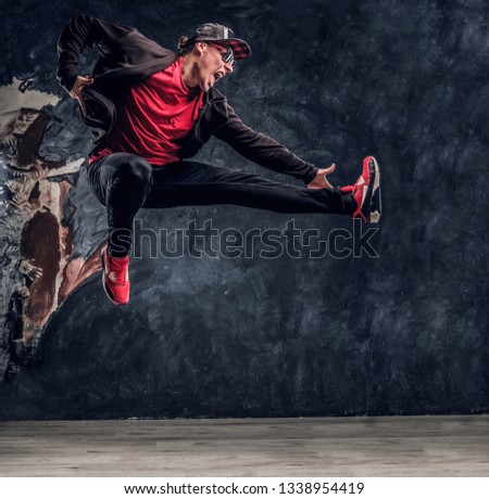 Emotional hip-hop style dancer performing dance elements. Studio photo against a dark textured wall
