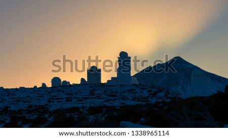 Sunset at the snowy observatory. Telescopes backlit with yellow sky and mount Teide in the background