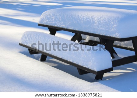 A brown wooden picnic table outdoors in a park is covered in a thick layer of freshly fallen snow.