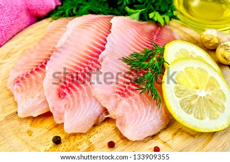 Tilapia fillets with dill, parsley, lemon, a bottle of vegetable oil, ginger, pink cloth, bell pepper on a wooden board Royalty-Free Stock Photo #133909355