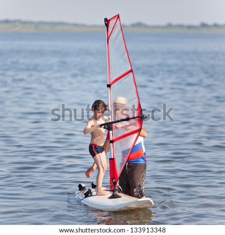 Little boy begins learning windsurfing and gets a lesson from a male instructor Royalty-Free Stock Photo #133913348