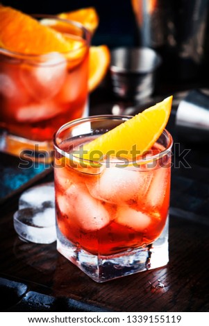 Summer alcoholic cocktail Negroni with dry gin, red vermouth and red bitter, orange slice and ice cubes. Brown bar counter background, bar tools, place for text, selective focus