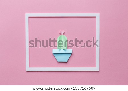 one small cute cactus of paper in the white frame on a pink background